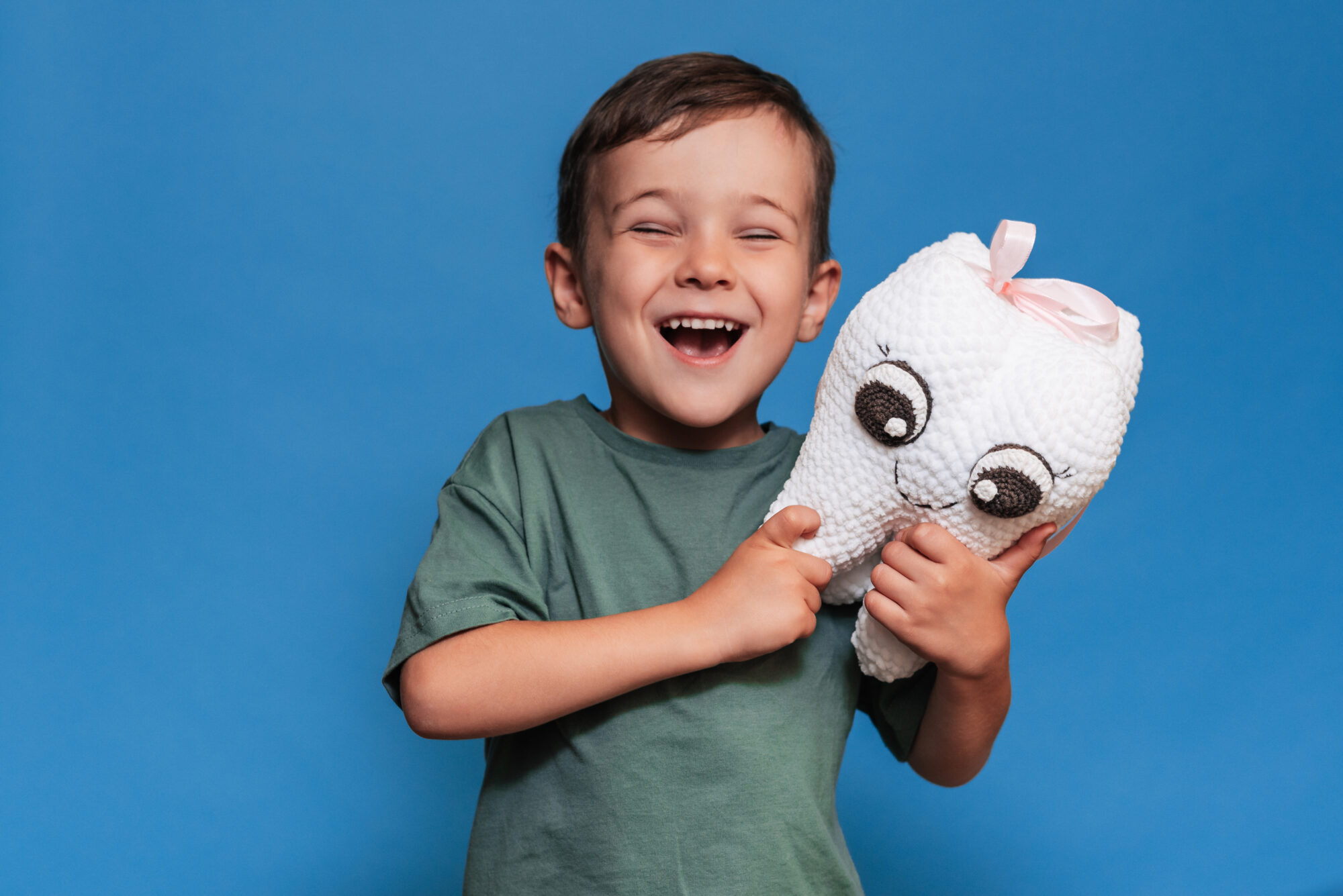 A smiling boy with healthy teeth holds a plush tooth on a blue background. Oral hygiene. Pediatric dentistry. Pediatric Dentist