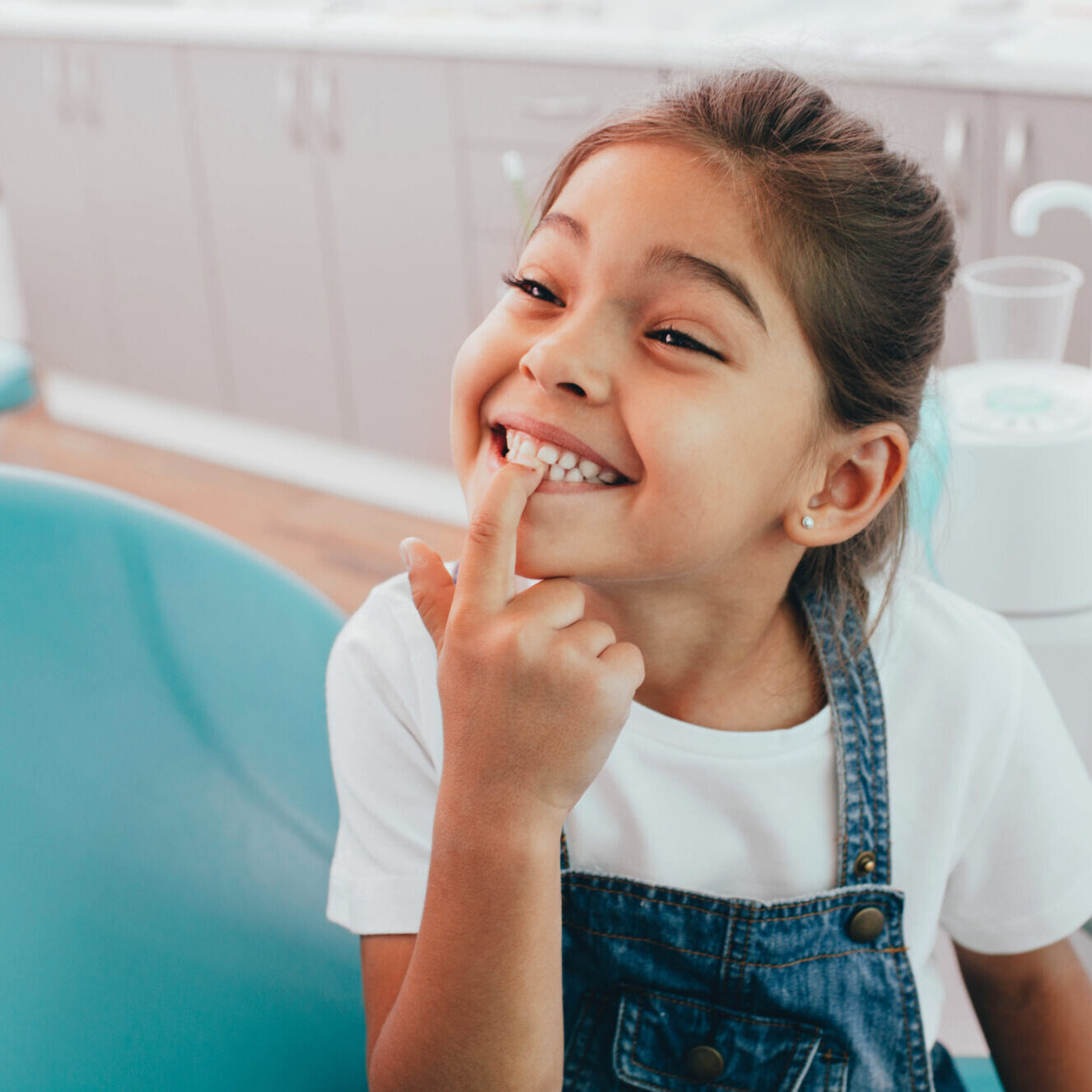 Mixed race little patient showing her perfect toothy smile while sitting dentists chair Katy Dentist Office
