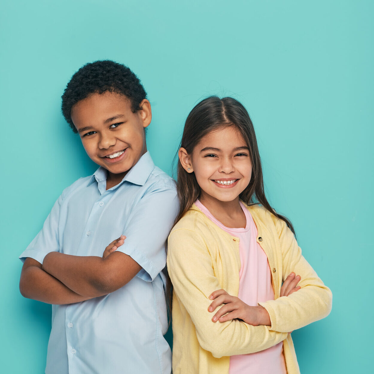 Asian girl and African American boy standing back to back with arms crossed on a turquoise background Katy Dentist Office